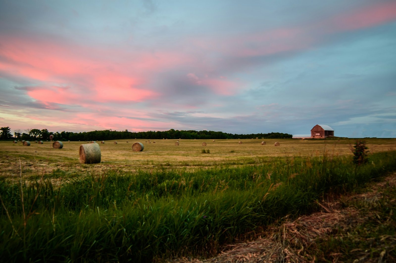 Scenic countryside landscape at sunset with hay bales on fields and barn farmhouse